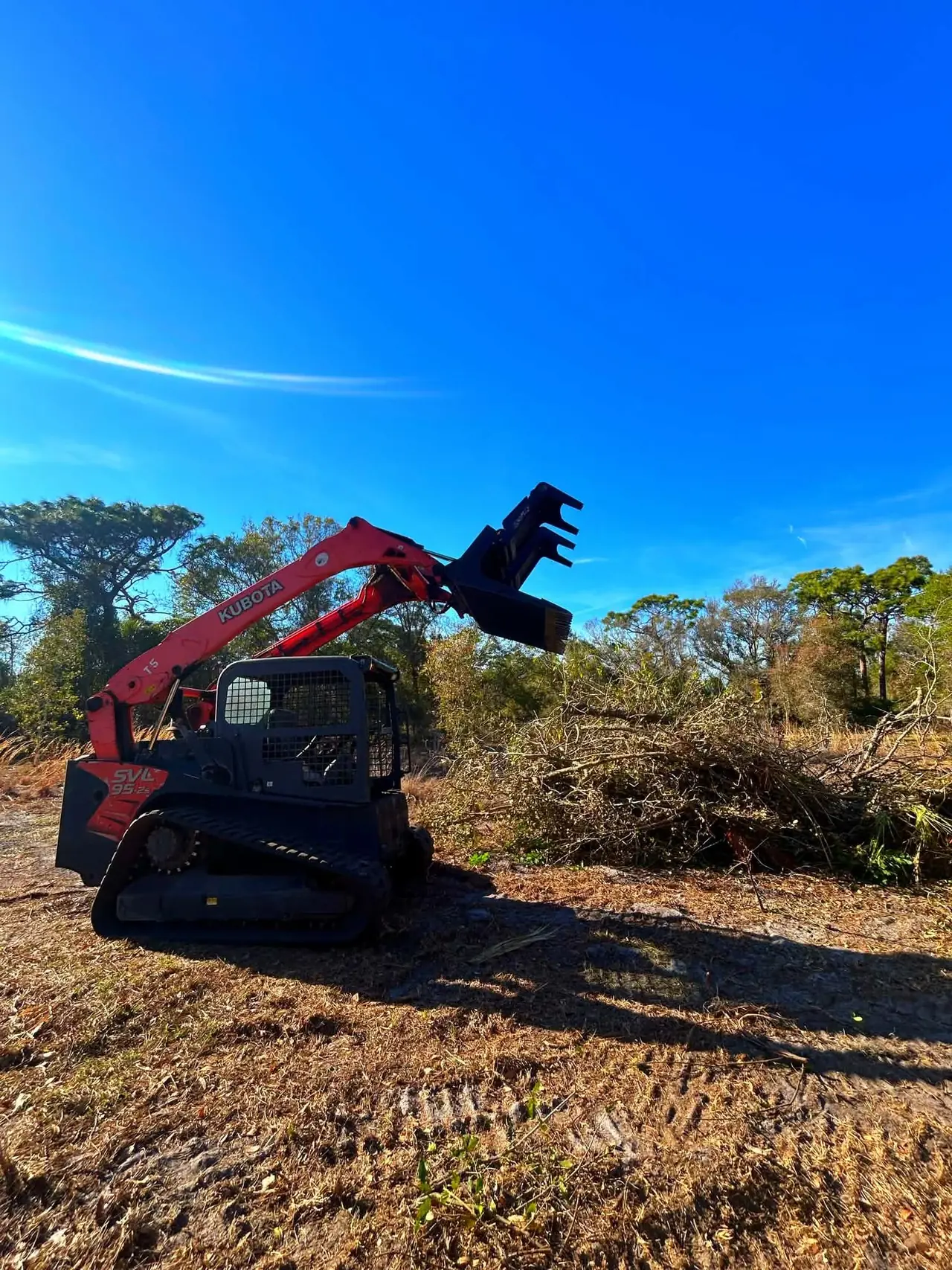 Landos Kubota SVL95 track loader clearing brush from a lot